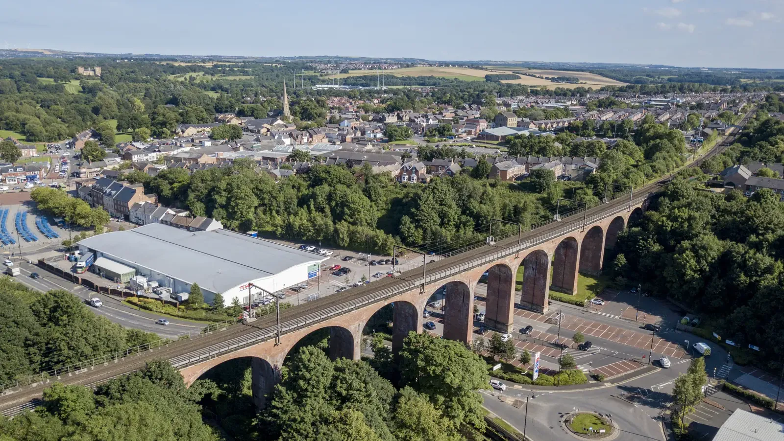 Aerial view of Chester-le-Street, with the railway viaduct crossing the foreground, the spire of the Church of St Mary and St Cuthbert above the town centre, and Lumley Castle in the trees beyond