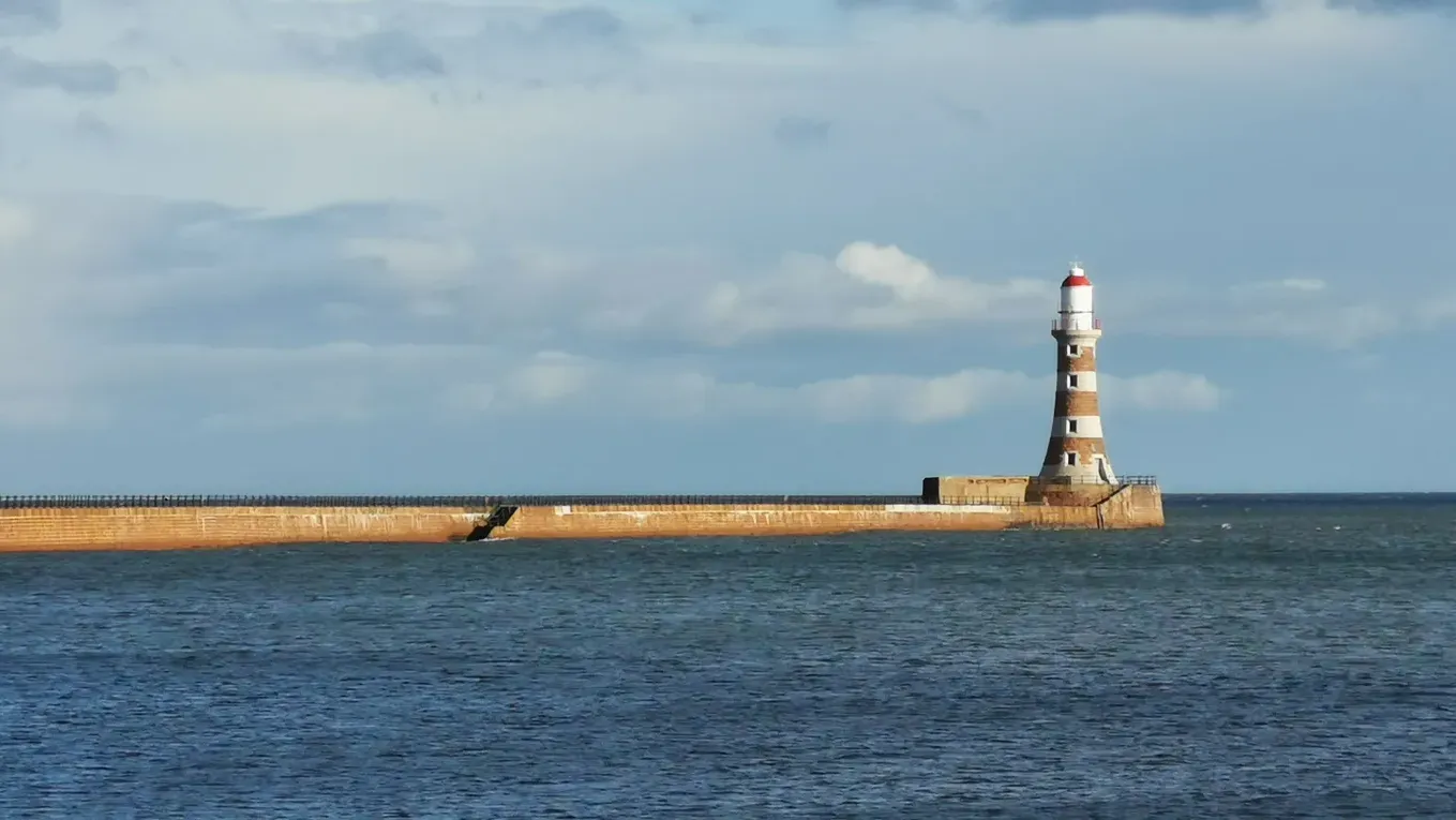 Roker Pier in Sunderland running out across a choppy North Sea to its red and white striped lighthouse, under a partly cloudy sky
