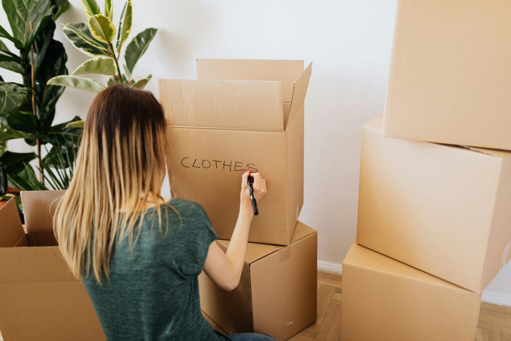 Woman labelling a cardboard box marked "Clothes" while packing